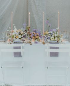 the table is set up with white chairs and purple napkins, candles and flowers