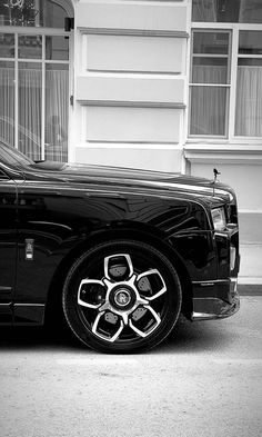 a black and white photo of a rolls royce parked in front of a building with windows