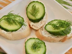 four pieces of bread with cucumbers and dill on them sitting on a plate