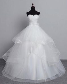 a white wedding dress on a mannequin stand in front of a gray wall