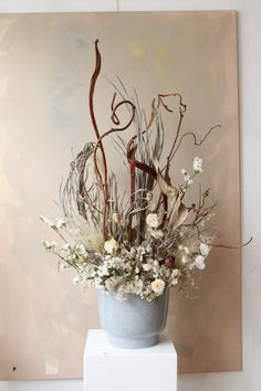 a blue vase filled with lots of flowers on top of a white pedestal next to a painting