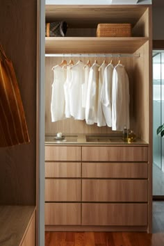 an open closet with clothes hanging on wooden shelves