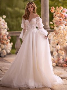 a woman in a wedding dress standing on a stone walkway with flowers and archways behind her