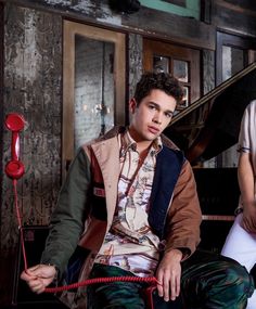 a young man sitting on top of a chair next to a red telephone cord and an old piano