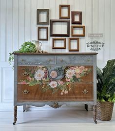 an old dresser with flowers painted on the front and sides, next to potted plants