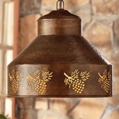 a hanging light with pineapples on it in front of a stone wall and potted plant