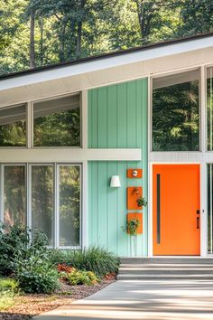 an orange front door is on the side of a green and white house with trees in the background