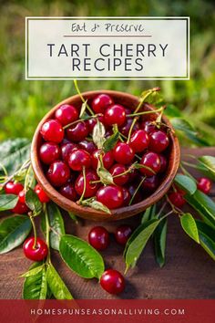 a bowl filled with cherries on top of a wooden table next to green leaves