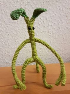 a green crocheted figure sitting on top of a wooden table next to a white wall