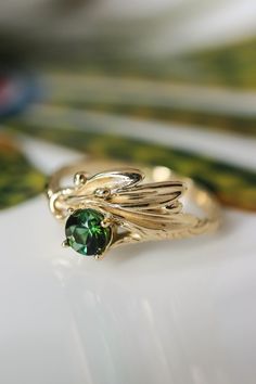 a close up of a ring with a green stone in the middle and gold leaves on it