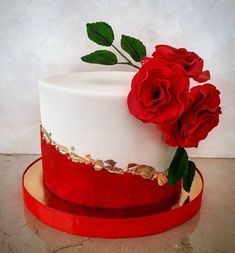 there is a white and red cake with two roses on the top, along with gold trimmings