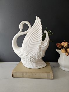 a white swan sculpture sitting on top of a book next to a vase with flowers