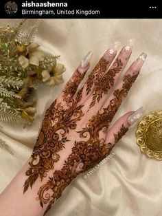 a woman's hand with henna on it next to flowers and a gold coin