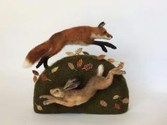 two stuffed animals laying on top of a green rock with leaves and acorns