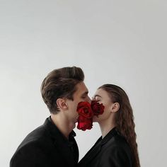 a man and woman kissing each other with red roses in front of their faces on a white background