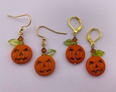 three pumpkin earrings with leaves on them are hanging from gold earwires that have carved jack - o'- lantern faces