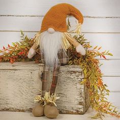 an orange and white knitted gnome sitting on top of a wooden box with leaves around it