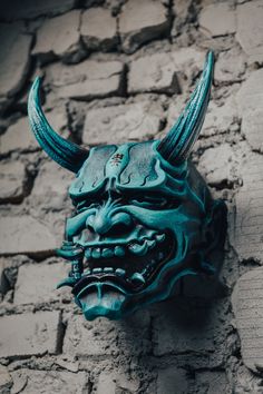 a green mask with horns hanging on a brick wall