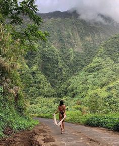 a woman walking down a dirt road holding a surfboard under her arm and wearing a bathing suit