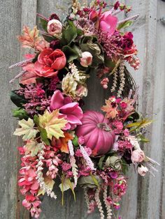 a wreath is hanging on the side of a wooden door with flowers and foliage around it