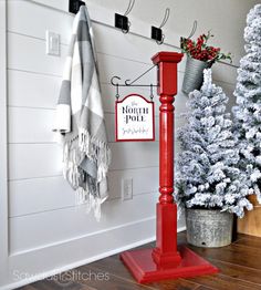 a white christmas tree sitting next to a red pole in front of a wall mounted clock