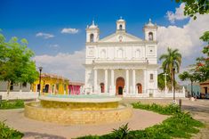 a white church with a fountain in front of it and palm trees around the corner