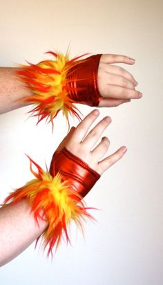 two hands with red and yellow feathers on their arms, one holding the other's hand