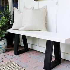 a white bench sitting on top of a wooden floor next to a rug and pillows