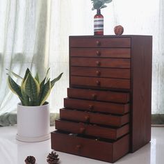 a wooden dresser sitting on top of a white table next to a potted plant