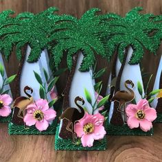 three decorative vases with flamingos and flowers in them on a wooden table next to a palm tree