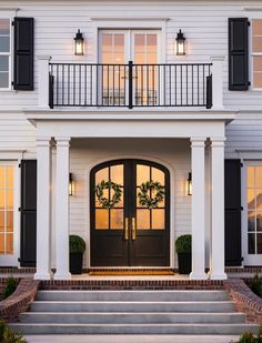 a white house with black shutters and two large doors on the front steps leading up to it