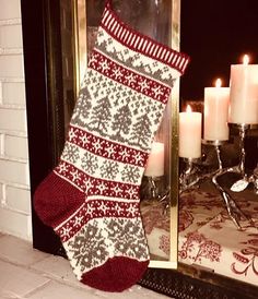 a red and white knitted christmas stocking next to a fireplace with candles in the background