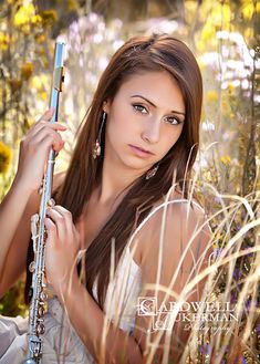 a beautiful young woman holding a flute standing in tall grass