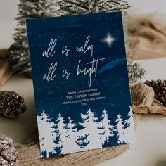 a card with the words all is easy, all is bright on it next to pine cones