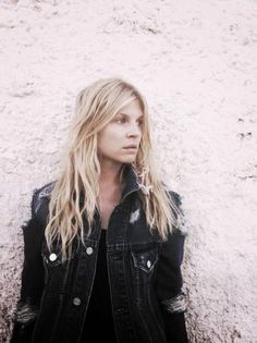 a woman standing in front of a white wall wearing a jean jacket and black dress