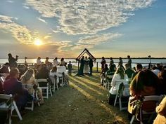 an outdoor ceremony with people sitting in chairs and facing the water at sunset or dawn