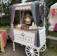 a white cart with purple and green decorations on it next to tables covered in gold cloths