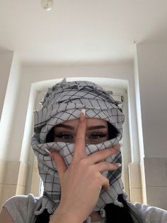 a woman wearing a scarf covering her face and making the v sign with her fingers