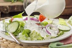 someone pouring dressing onto a salad on a plate