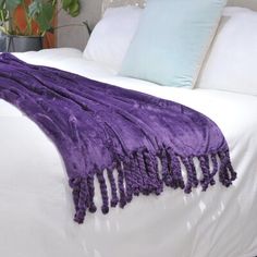 a white bed topped with purple blankets and pillows