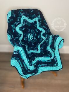 a blue crocheted blanket sitting on top of a wooden floor next to a chair