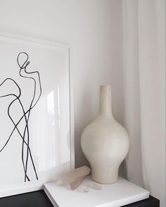 a white vase sitting on top of a table next to a black and white painting