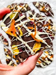 a person holding up a piece of chocolate with fruit and white icing on it