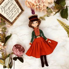 the doll is wearing a red dress and green jacket with feathers on it's head