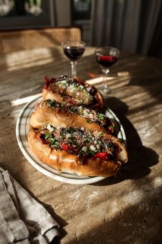 two hot dogs sitting on top of a white plate next to a glass of wine