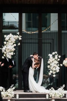 a bride and groom kissing in front of their wedding arch with white flowers on it