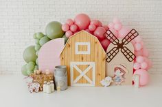 a table topped with balloons and farm animals next to a wall covered in pink, green, and white balloons