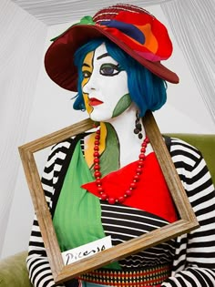 a woman with blue hair wearing a clown mask and holding a framed photo in her hands