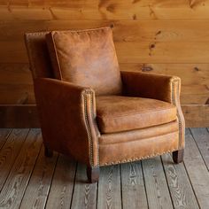 a brown leather chair sitting on top of a wooden floor next to a wood wall