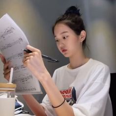 a woman sitting at a table writing on a piece of paper while holding a pen